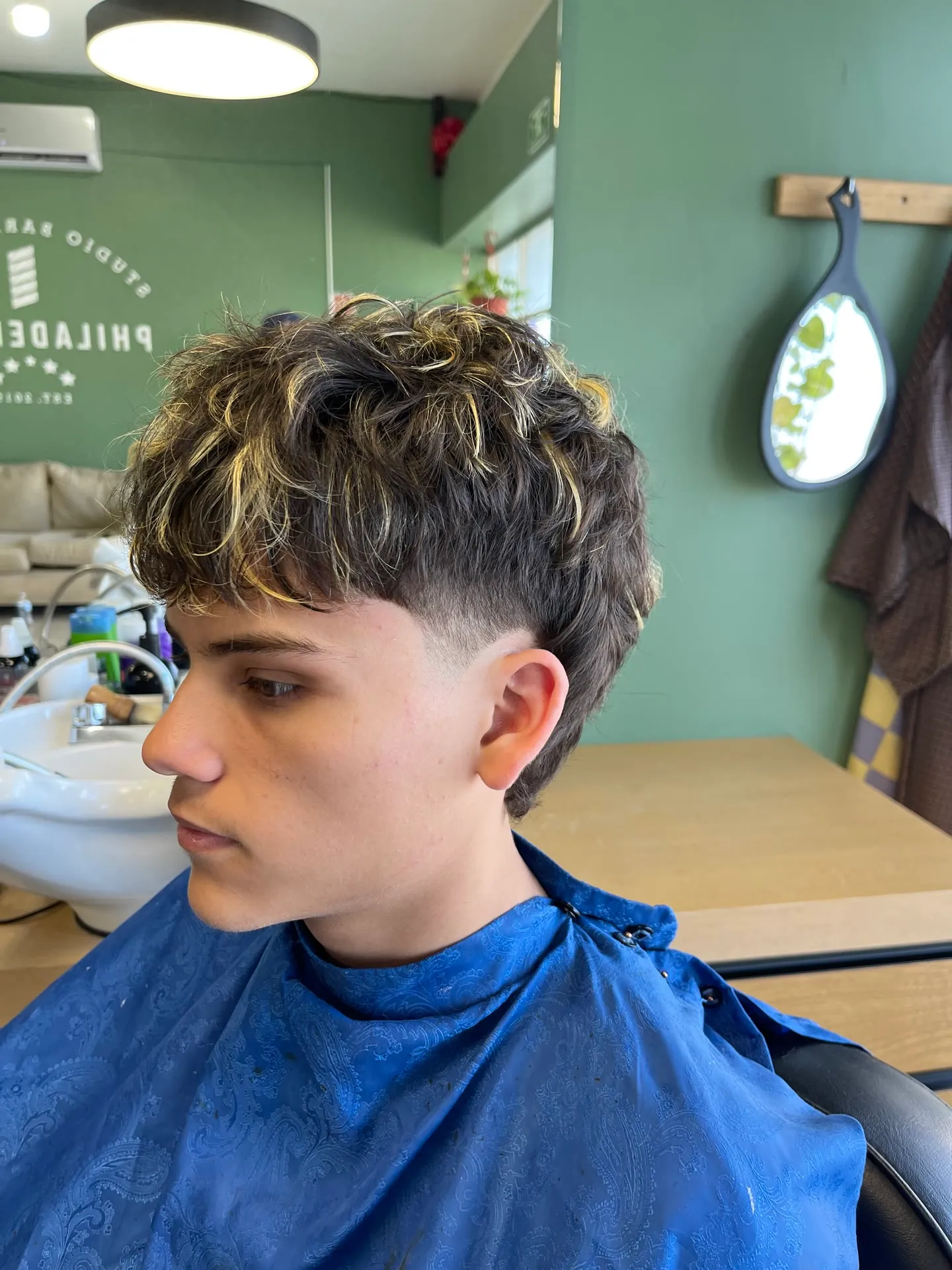 Mullet rizado con mechas rubias y laterales desvanecidos